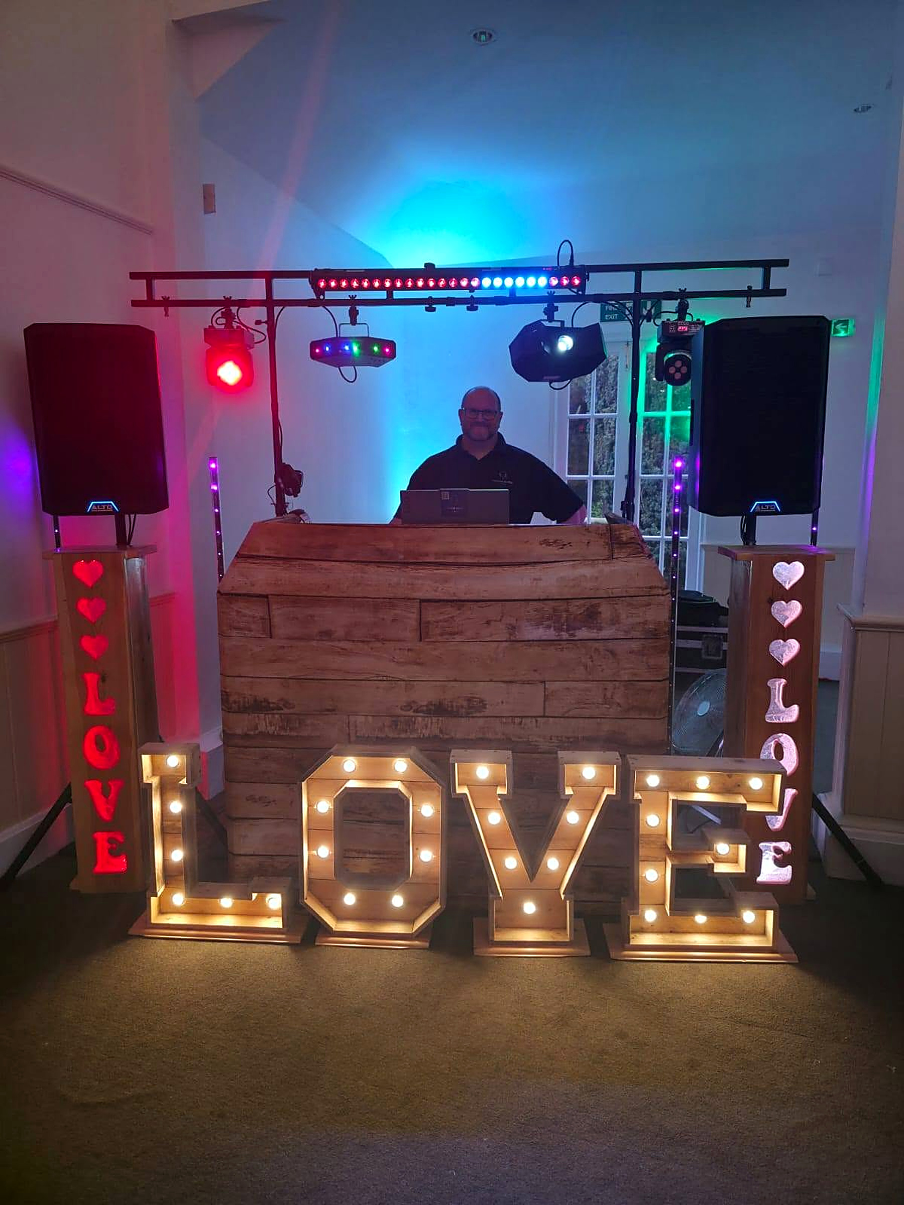 Luxton Music DJ setup with lighting rig, speakers and illuminated LOVE letters at a wedding reception